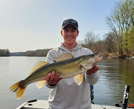 Man holding a large walleye he just caught while standing in a boat on a river